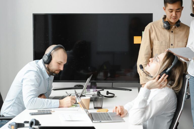 Employees in a modern office setting working with headsets and laptops, demonstrating teamwork and communication.