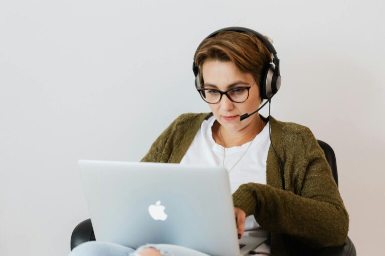 Woman wearing glasses and headset working on a laptop, focused and productive.